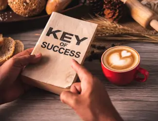 Hands holding a book titled 'Key of Success' next to a cup of coffee, representing it as a tool for business growth and success.