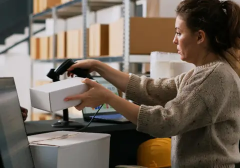 A woman managing inventory on a computer in a warehouse setting, illustrating real-time inventory tracking with ERP software.