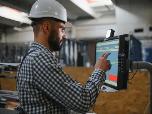 Factory worker using manufacturing software for small businesses on a touchscreen device to manage production operations.