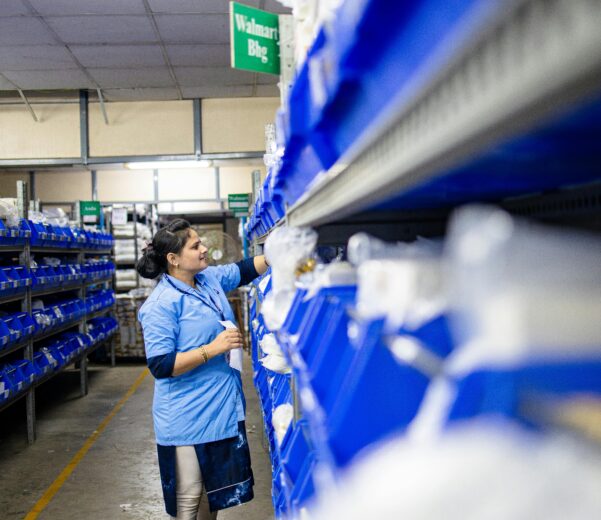 A woman in a warehouse organizes inventory shelves with labeled bins.