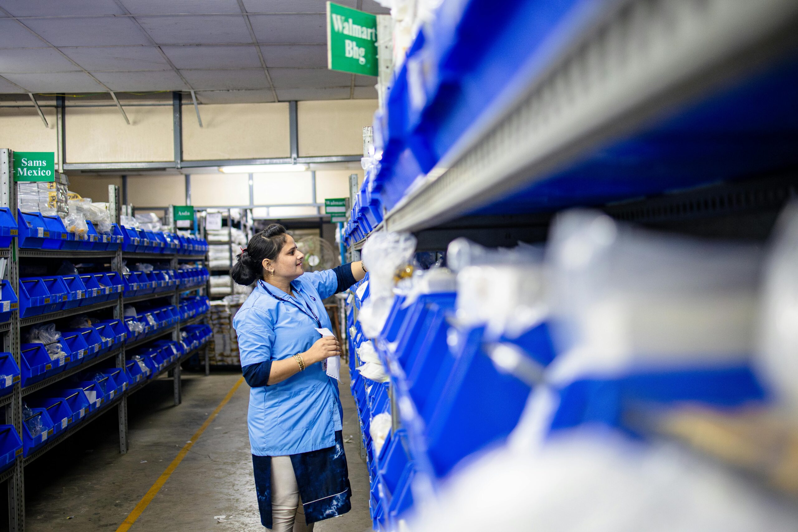 A woman in a warehouse organizes inventory shelves with labeled bins.